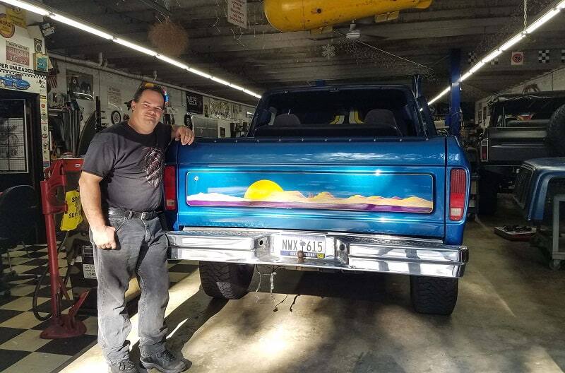 Man posing next to trunk of the blue Bronco in garage