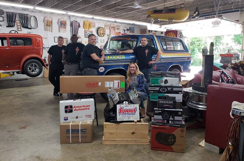 Bronco girl with mechanics posing in front of blue Bronco with various car part boxes