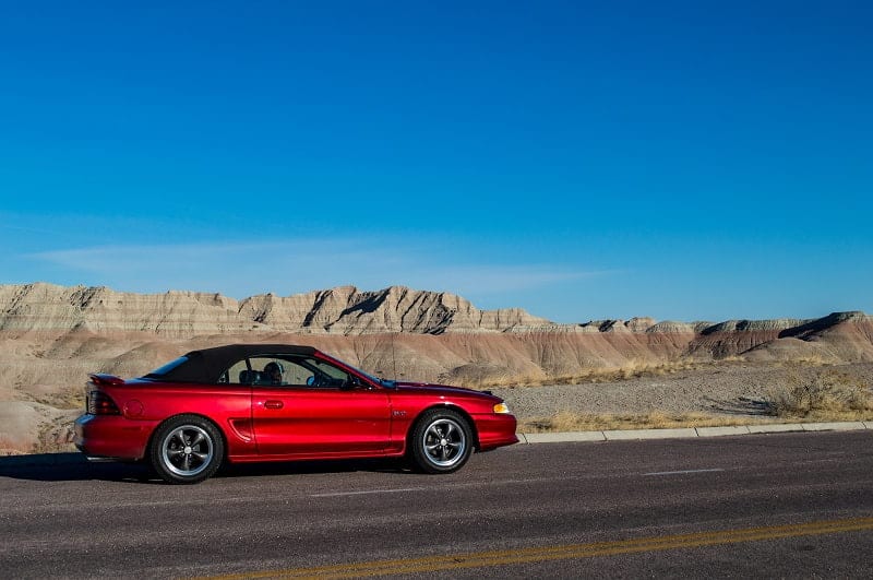 Profile of red Mustang on the road with mountains in the back