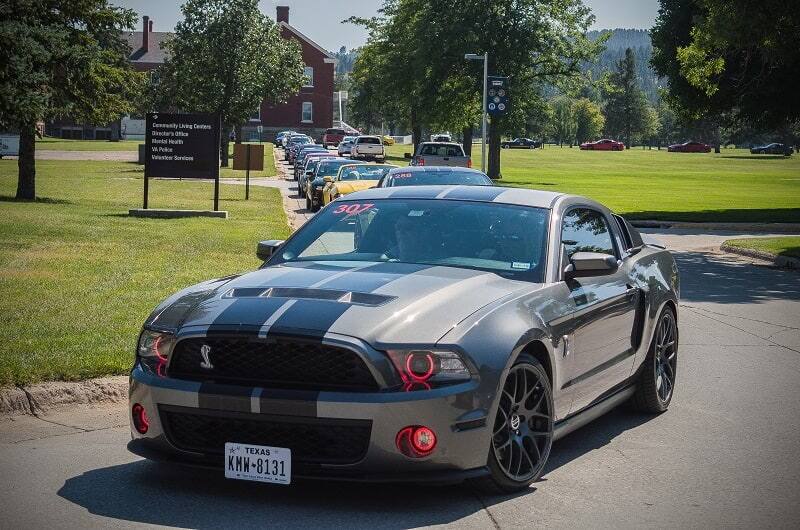Front of gray Shelby Mustang leading a pack of other Mustangs on the road