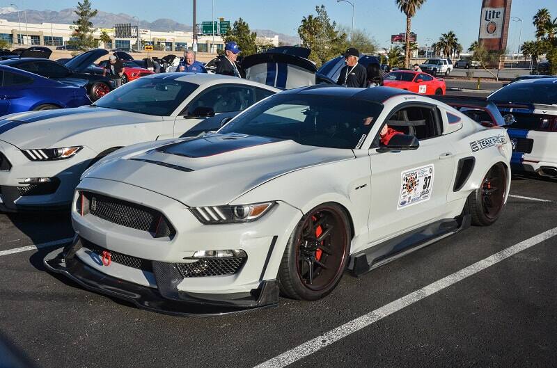 Front profile of white Shelby Mustang in parking lot with various other Shelbys