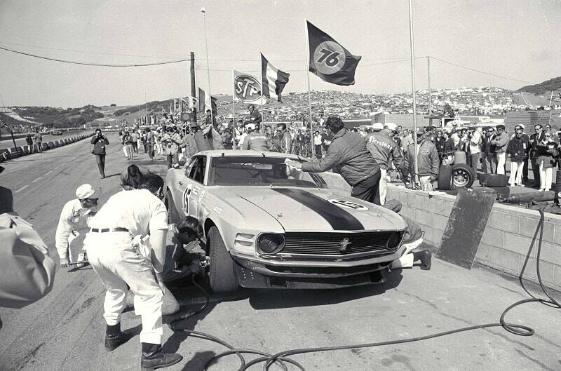 Black and white image of mechanics working on a Mustang at the pit stop on a track