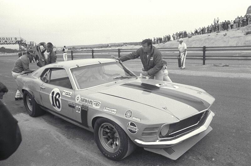 Black and white image of a man wiping down a Mustang on the side of a track