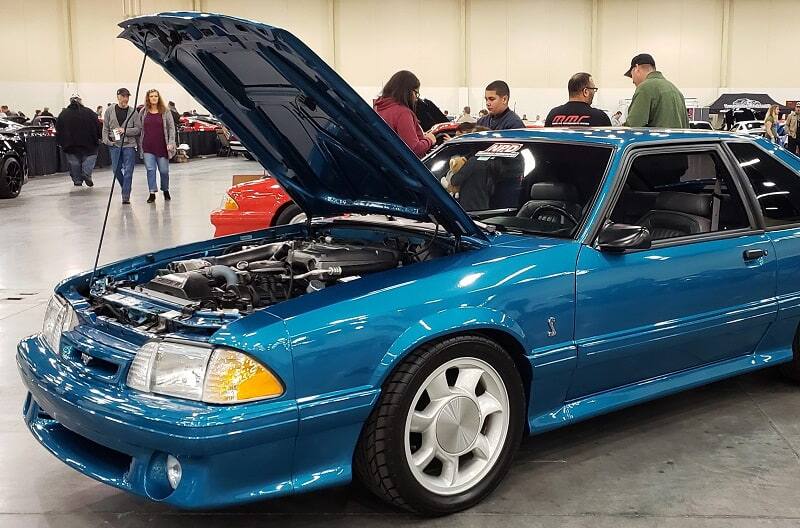 Front end profile of blue Shelby Mustang with hood up in garage