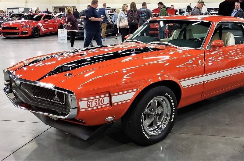 Close up front end of red Mustang GT 500 in garage with people and other Fords behind it