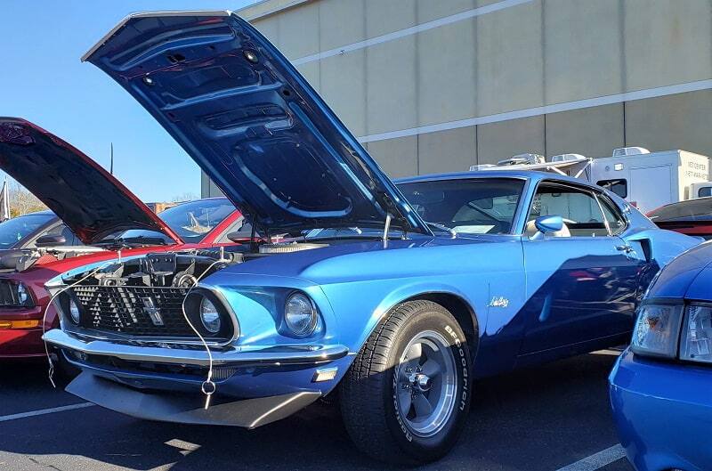 Close up front of blue Mustang with hood up outside of building