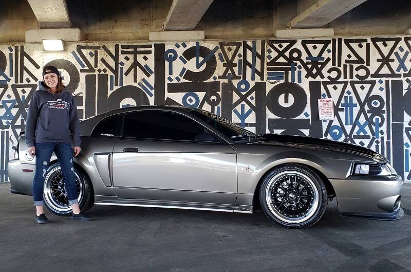 Girl pictured with profile of gray Mustang under bridge