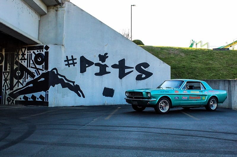 Profile of teal Mustang in front of overpass