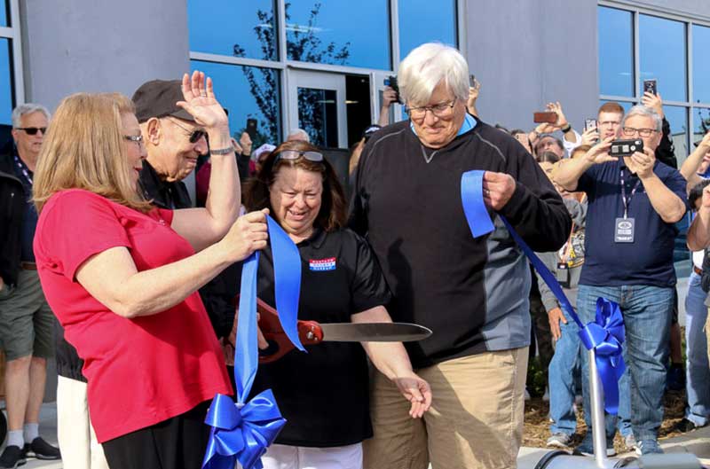 Woman cutting blue ribbon with crowd of people surrounding