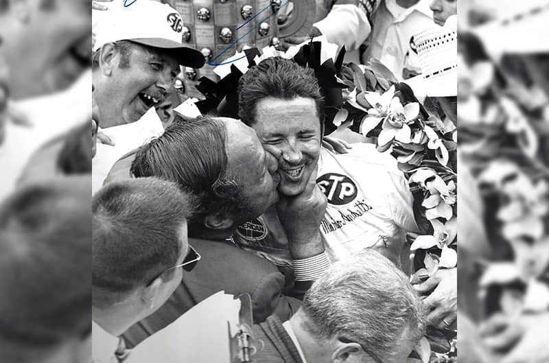 Black and white photo of Granatelli kissing Andretti on the cheek on victory lane
