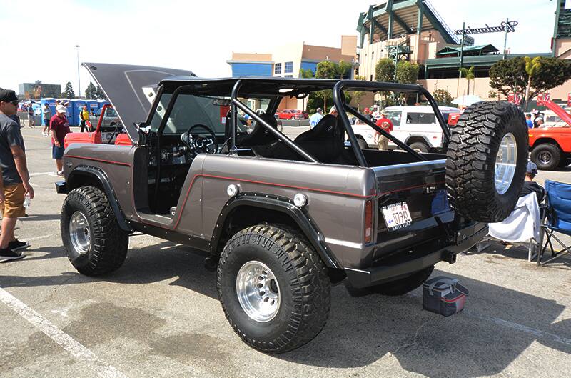 Rear profile of gray Bronco with doors and windows off and hood up in parking lot