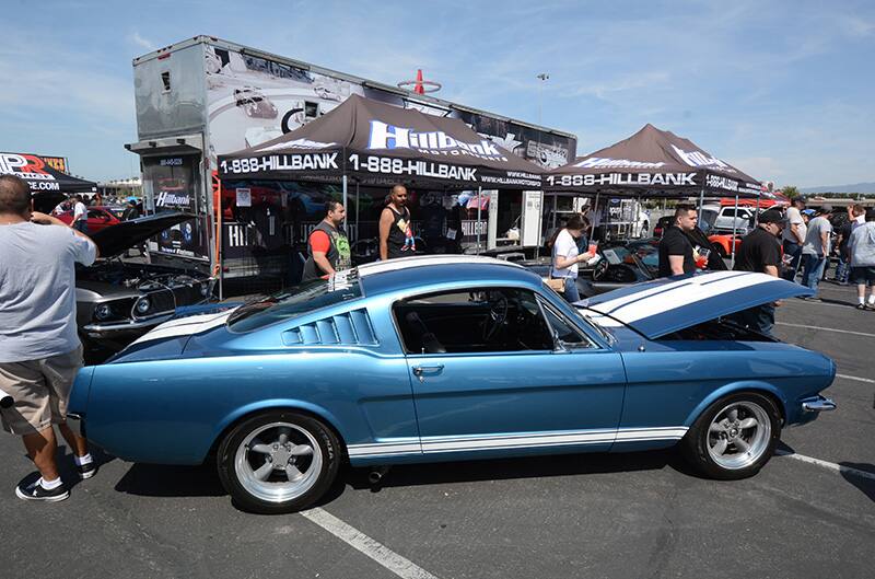 Profile of blue Mustang with hood up in parking lot in front of small tents and people