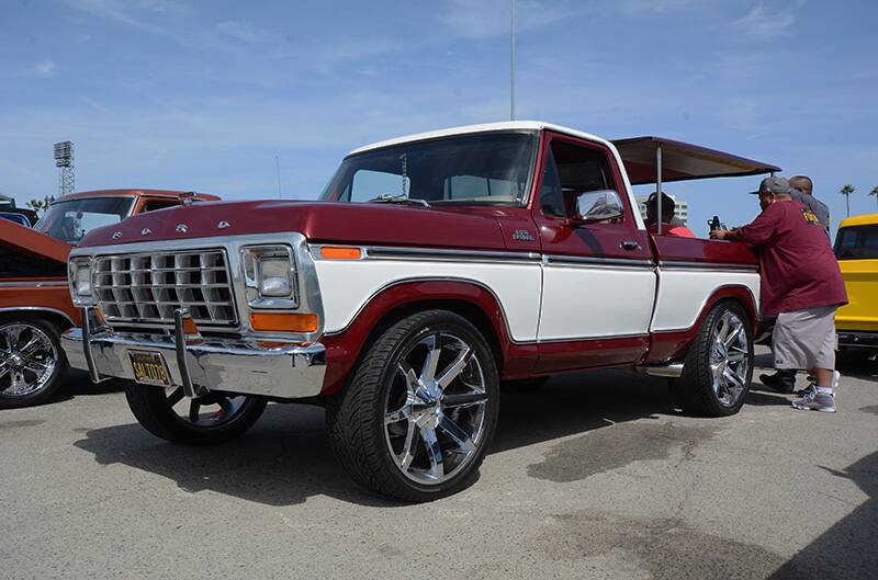 Front profile of red with white striped Ford truck in parking lot with man leaning over the trunk