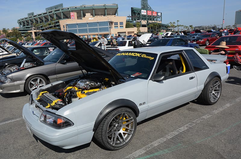 Profile of white Mustang with hood up in parking lot full of Fords