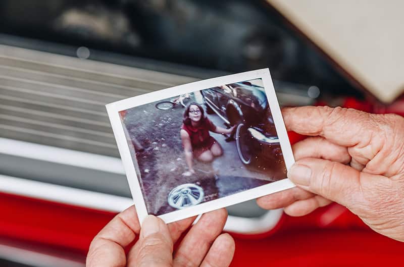 Hands holding up an old photo of young girl next to the red Mustang