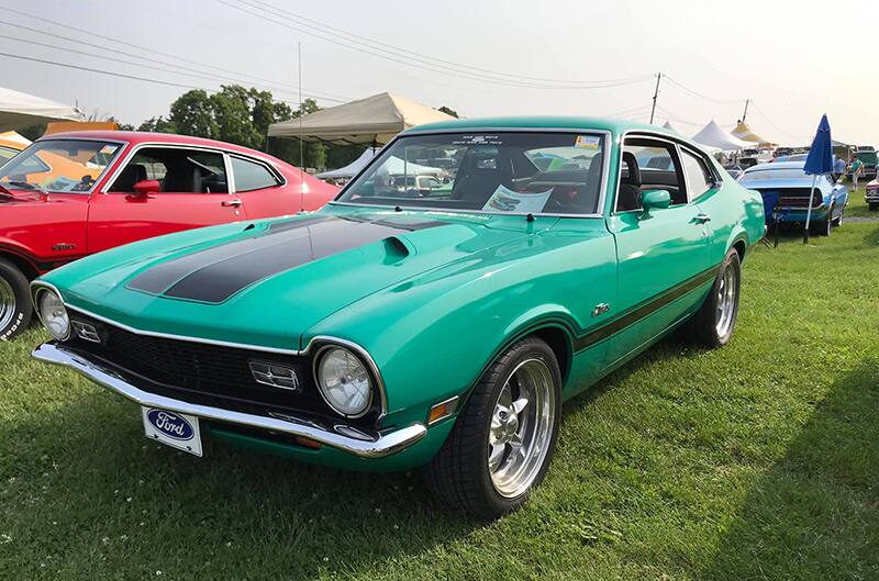 Front profile of a green Mustang with black stripe on hood parked on grass