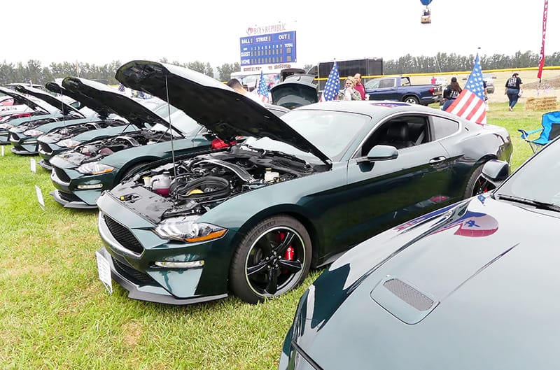 Profile of various green Mustangs with hoods open in a line on the grass