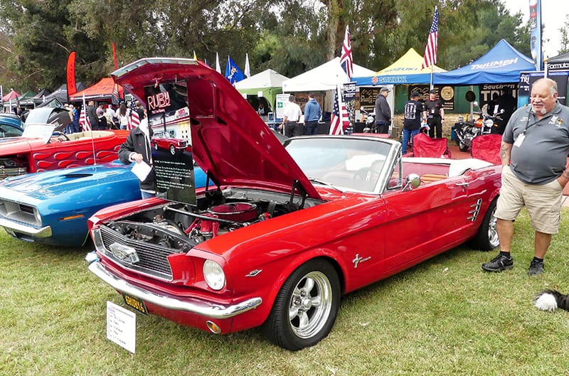 Profile of Ruby Red Mustang droptop with hood open and roof down on the grass