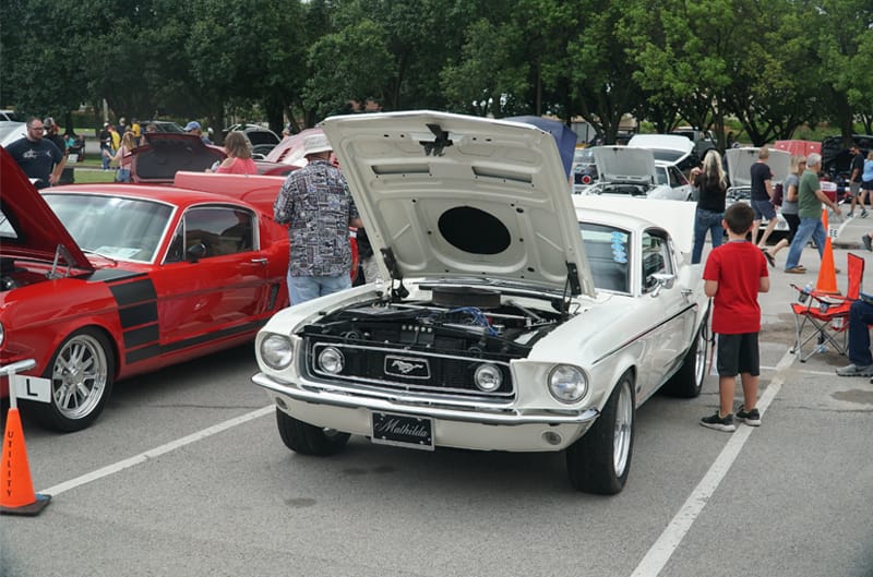 Front of a white Mustang with hood and trunk open in parking lot