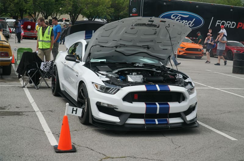 Front of white Shelby Mustang with blue stripes with hood and trunk open in parking lot