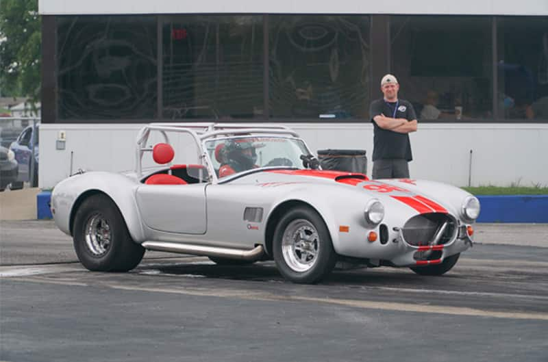 Front profile of a silver Shelby Roadster with red stripes in the parking lot