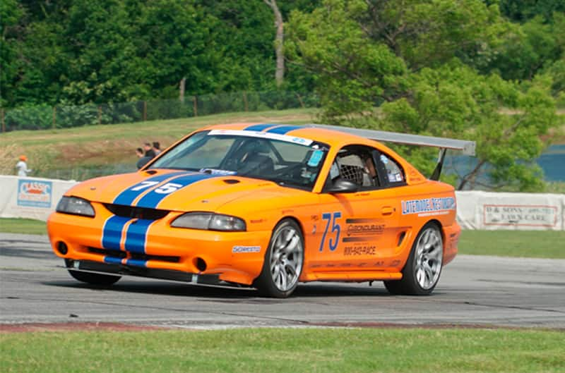 Front profile of orange with blue stripes Mustang on the track