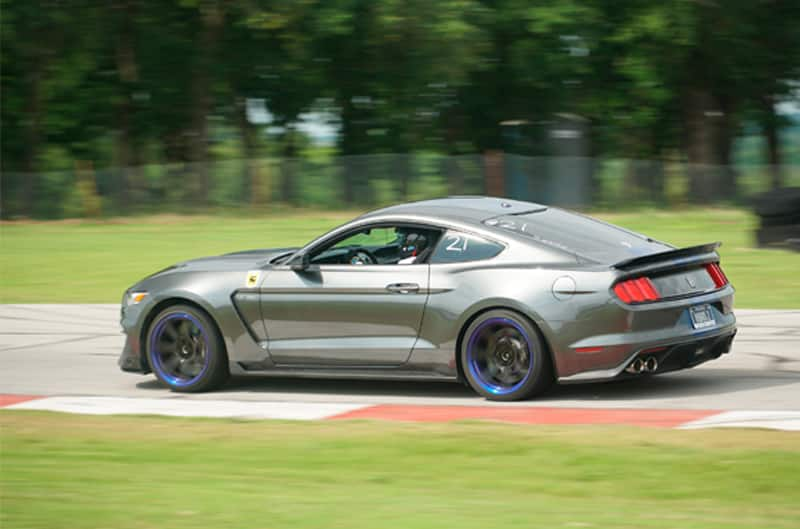 Profile of a dark gray Mustang driving on the track