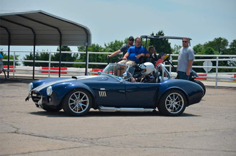 Profile of blue Shelby Roadster in a parking lot with people around it