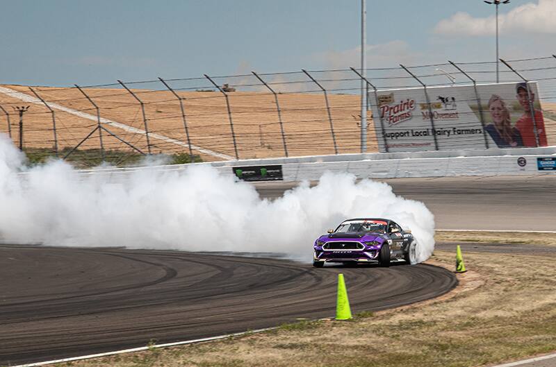 Front of Chelsea DeNofa drifting his black Mustang on the track