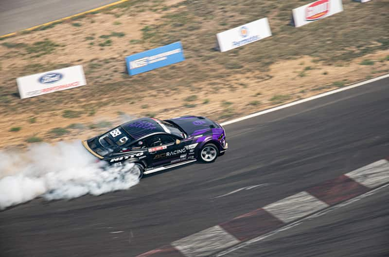 Overhead profile shot of Chelsea DeNofa drifting his black Mustang on the track