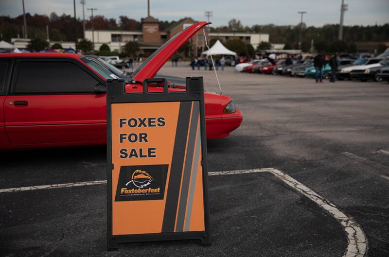 Sign that reads Foxes for sale in front of the profile of a red Mustang with hood open in parking lot