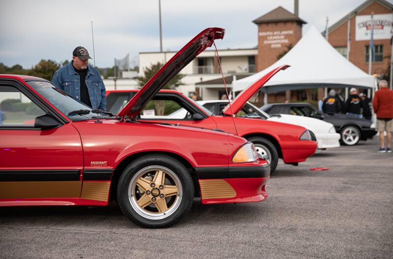 Profile of front ends of red and white Mustangs in parking lot