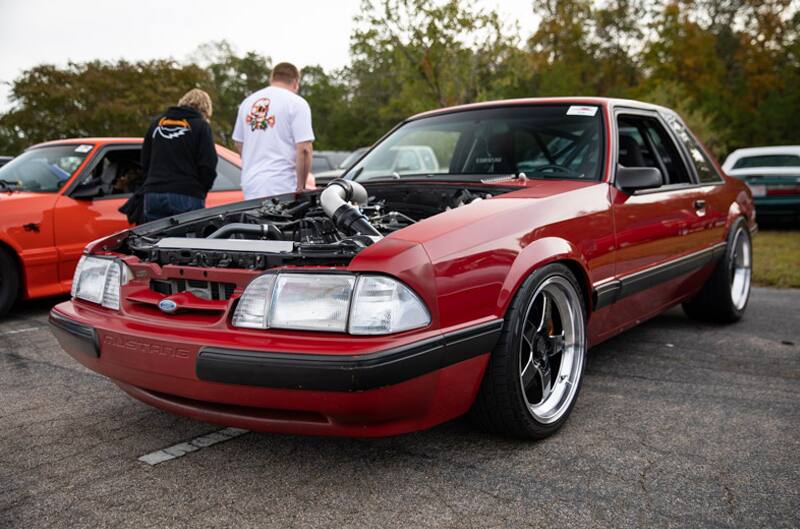 Front profile of red Mustang with hood off in parking lot