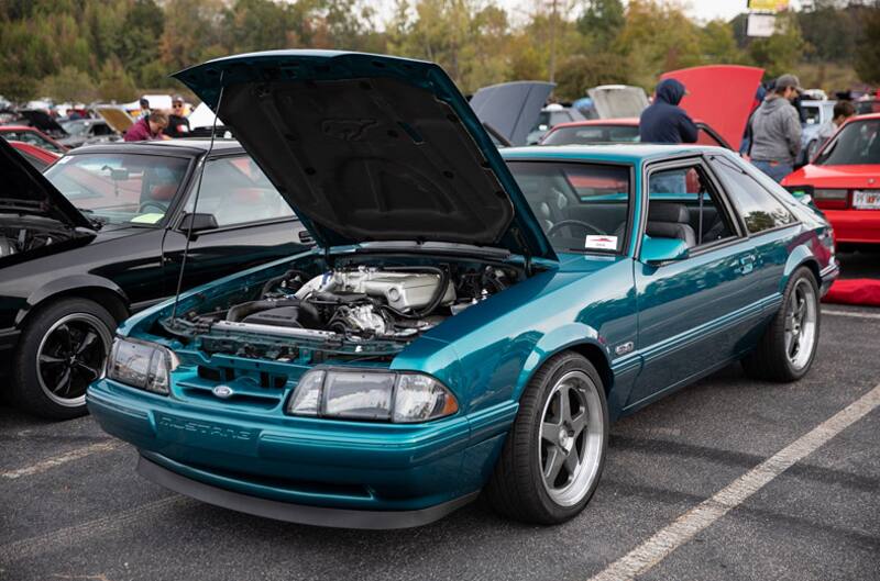 Front profile of teal blue Mustang with hood open in parking lot