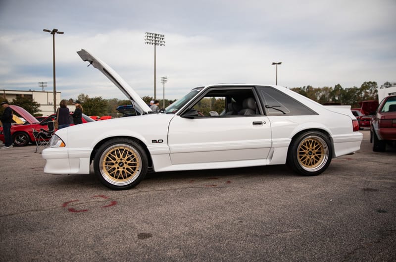 Profile of white Mustang with hood open in parking lot