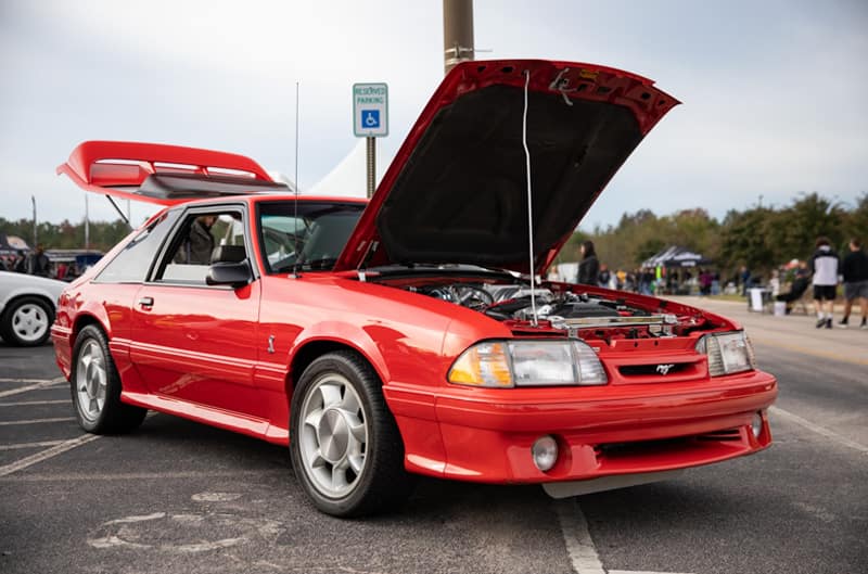 Front profile of red Mustang with hood and trunk open in parking lot