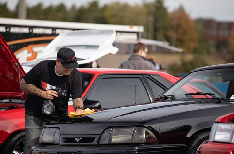 Man wiping down the hood of a black Mustang