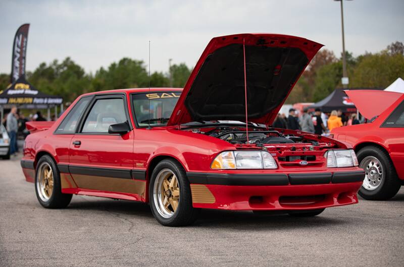 Front profile of red Mustang with hood open in parking lot