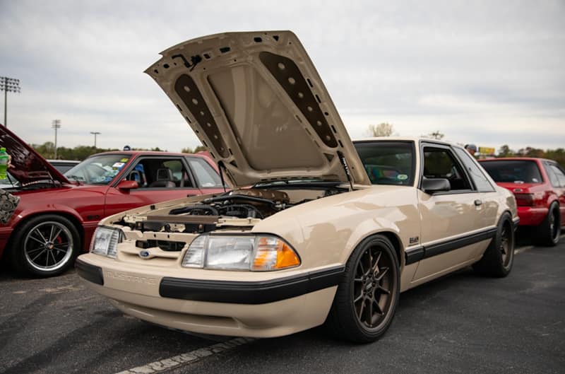 Front profile of cream Mustang with hood open in parking lot