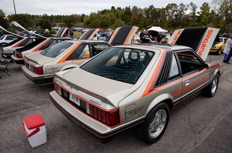 Various gold Mustangs in the parking lot with hoods open