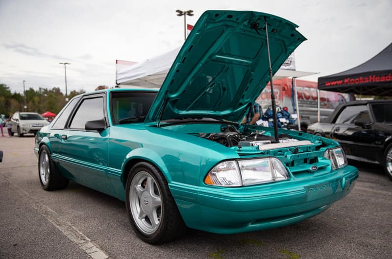 Front profile of teal green Mustang with hood open in parking lot