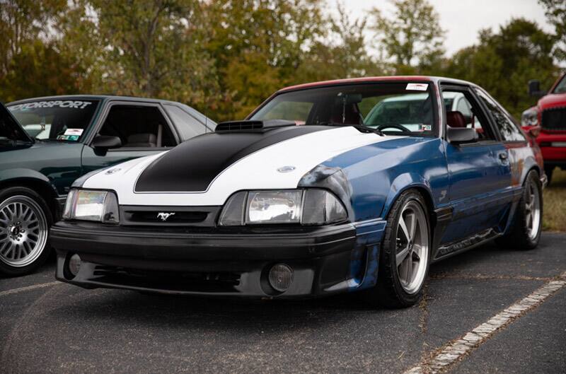 Front of blue Mustang with white and black hood in parking lot