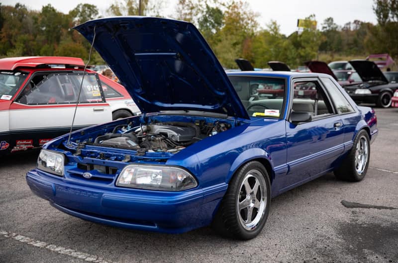 Front profile of blue Mustang with hood open in parking lot