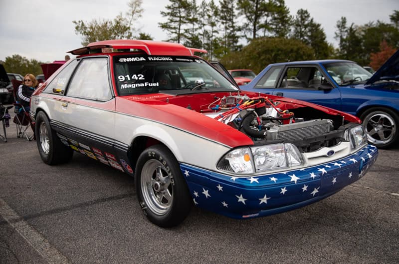 Front profile of a red white and blue flag themed Mustang with hood off in parking lot