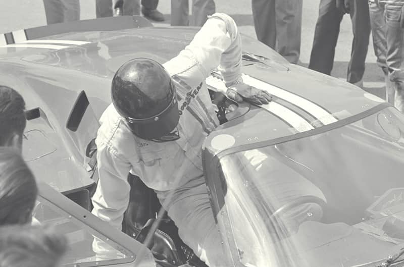 Black and white photo of Dan Gurney getting into his Ford GT40