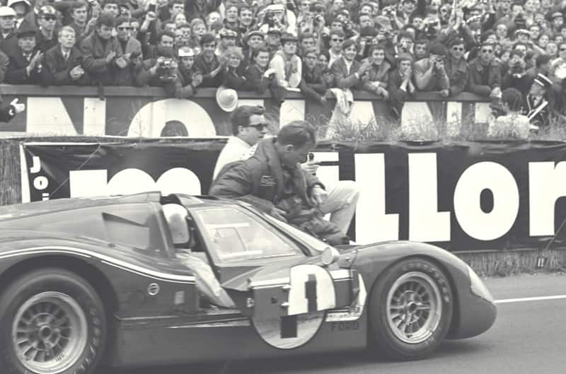Black and white close up of Dan Gurney sitting on his GT with a crowd of people in the stands