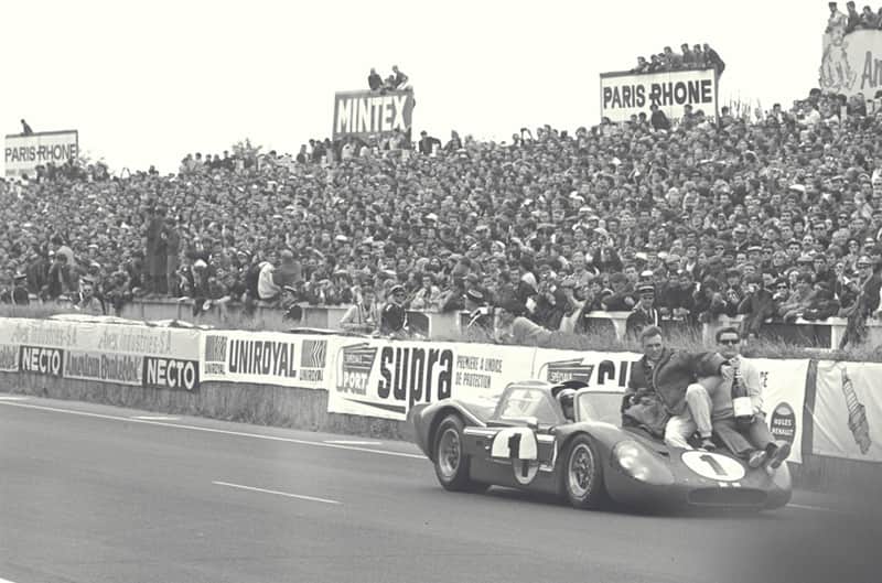Black and white front view of Dan Gurney sitting on his GT with a crowd of people in the stands