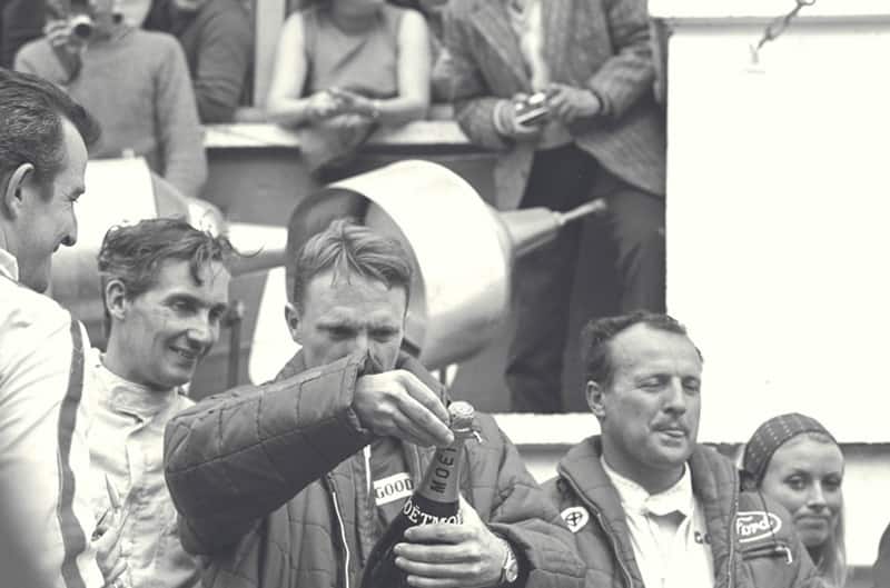 Black and white photo of Dan Gurney opening a bottle of champagne