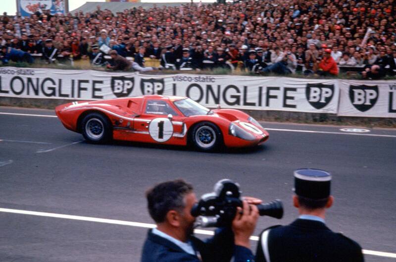 Profile of red GT driving on the track with crowd of people in the stands