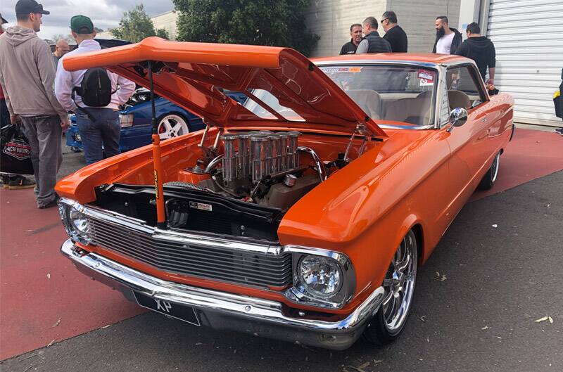 Front profile of orange Mustang on display in parking lot with hood open